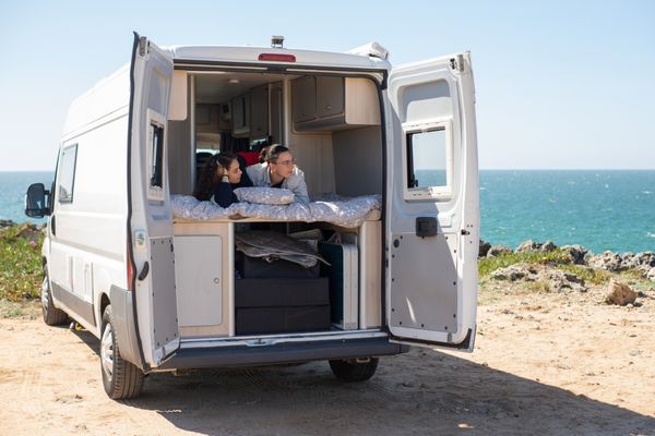 Ein Wohnmobil mit offener Heckklappe in de zwei Personen in einem Bett liegen und rausschauen.
